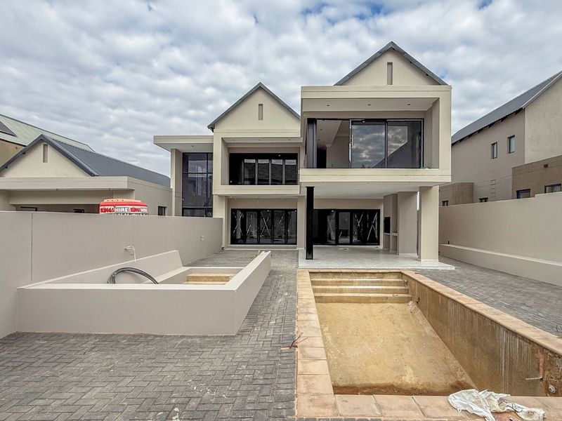 Rear view of a modern double-story house featuring a paved patio, balcony, and an unfinished swimming pool area.