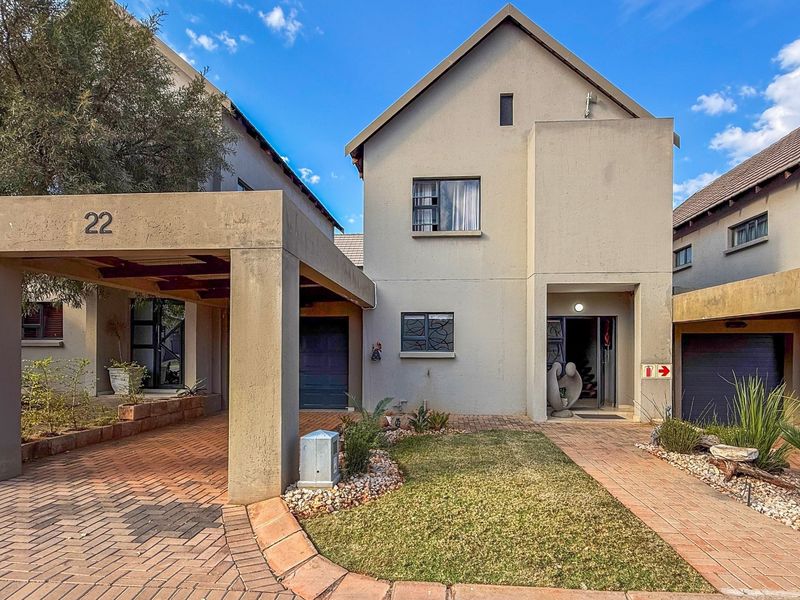 Front elevation of a townhouse featuring a paved driveway, covered carport, and a neat garden entrance with security gate.