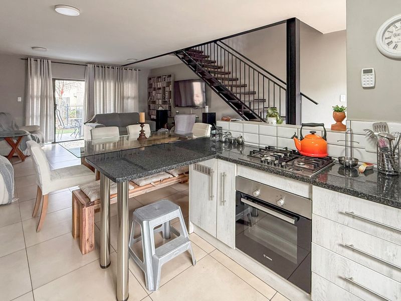 Open-plan living area featuring a modern kitchen with granite countertops, gas hob, and built-in oven, flowing into a dining space with staircase access.