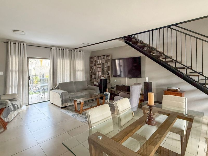 Spacious open-plan living and dining area featuring tiled floors, a modern metal staircase, and large sliding doors leading to the outdoor patio.