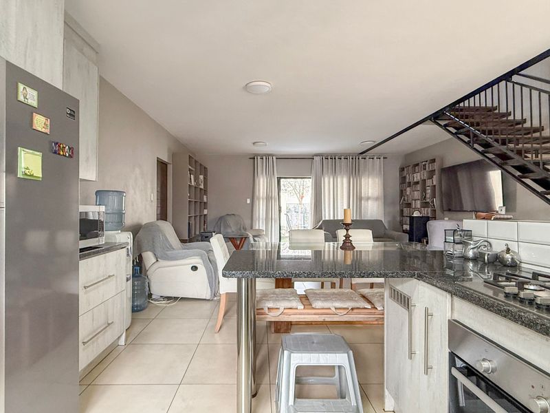 Open-plan living area featuring a modern kitchen with granite countertops, gas hob, and built-in oven, flowing into a spacious lounge with staircase access.