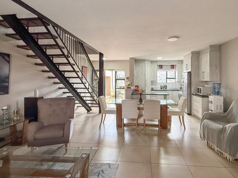 Spacious open-plan living and dining area featuring a modern open-tread staircase, tiled floors, and a functional kitchen with ample cabinetry.