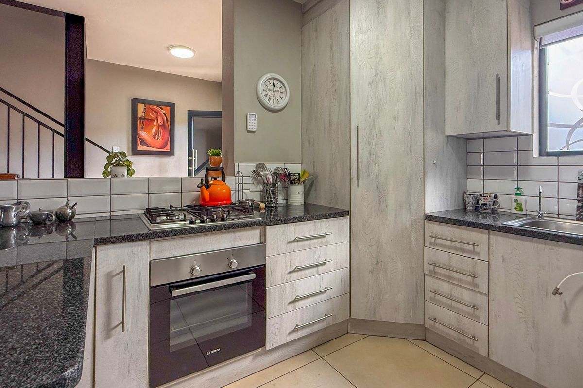 Modern kitchen featuring light wood-grain cabinetry, granite countertops, a built-in gas hob, and an integrated oven, with a clean tiled backsplash.