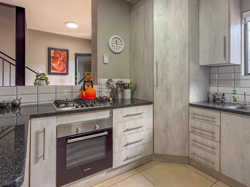 Modern kitchen featuring light wood-grain cabinetry, granite countertops, a built-in gas hob, and an integrated oven, with a clean tiled backsplash.