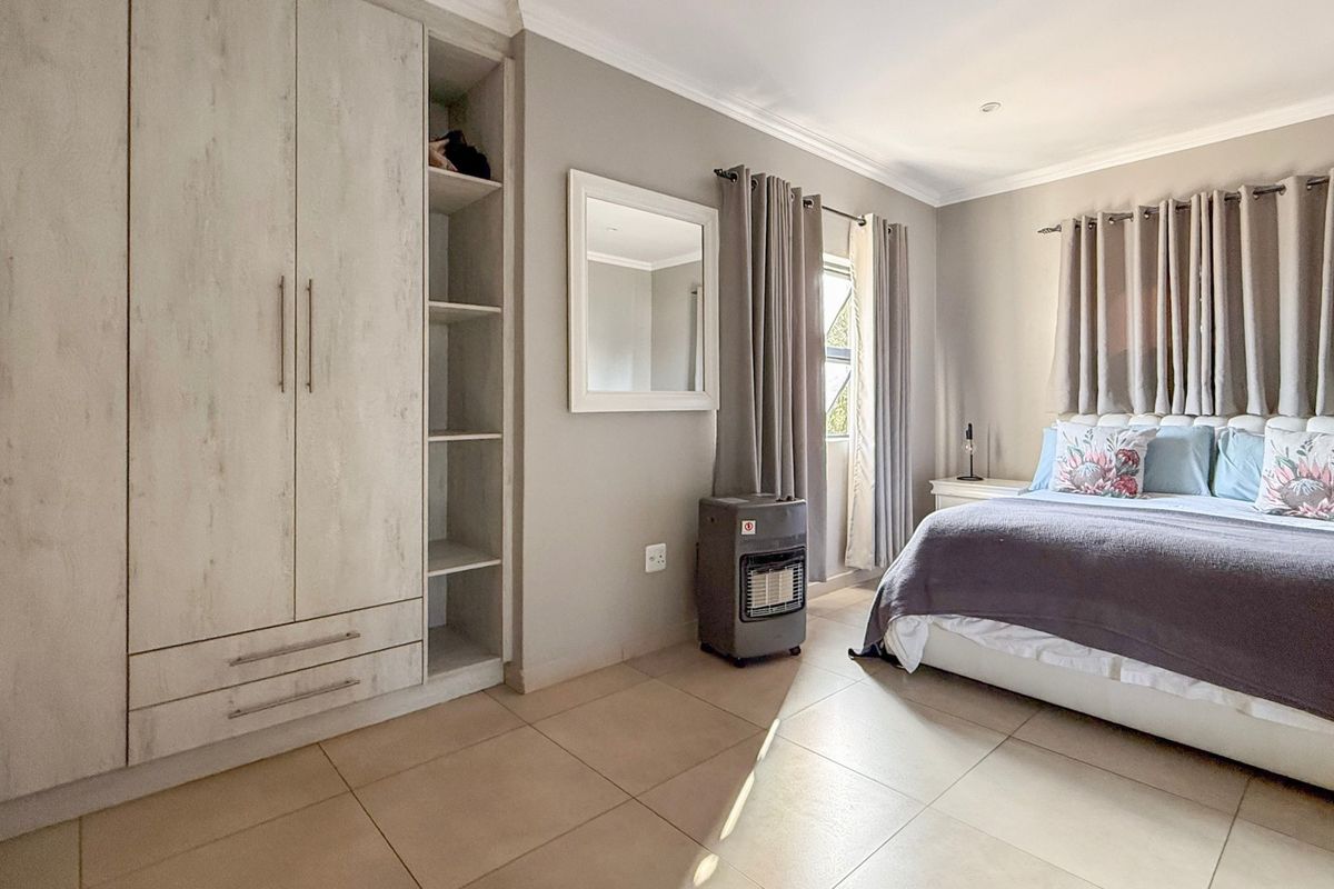A well-maintained bedroom featuring neutral tiled flooring, built-in cupboards with open shelving, and soft grey wall finishes.