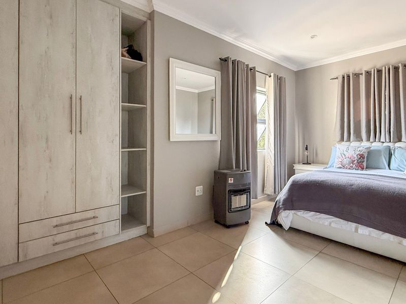 A well-maintained bedroom featuring neutral tiled flooring, built-in cupboards with open shelving, and soft grey wall finishes.