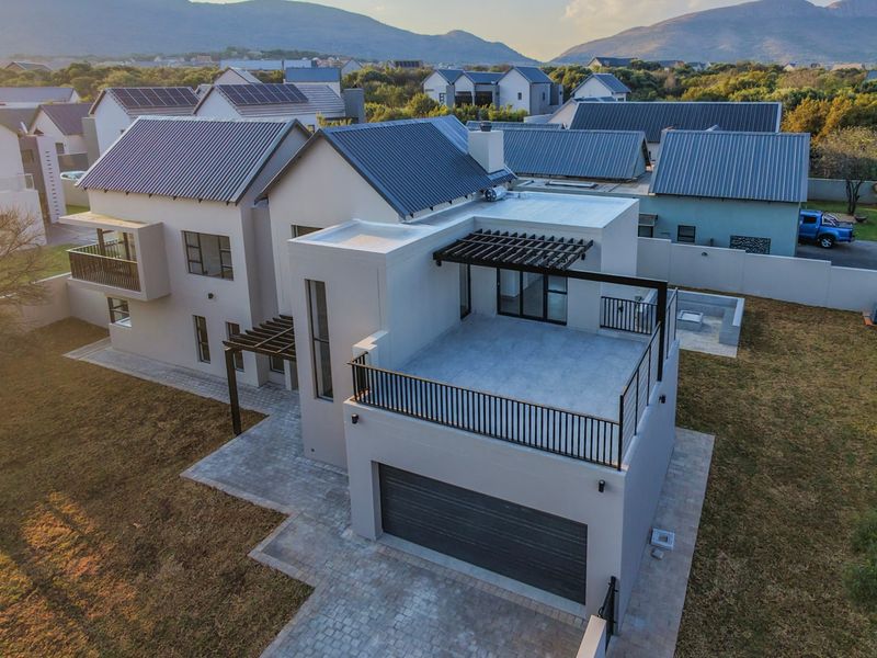 Aerial view of a modern double-story residential property featuring a metal roof, balcony, garage, and paved outdoor areas within a secure estate.