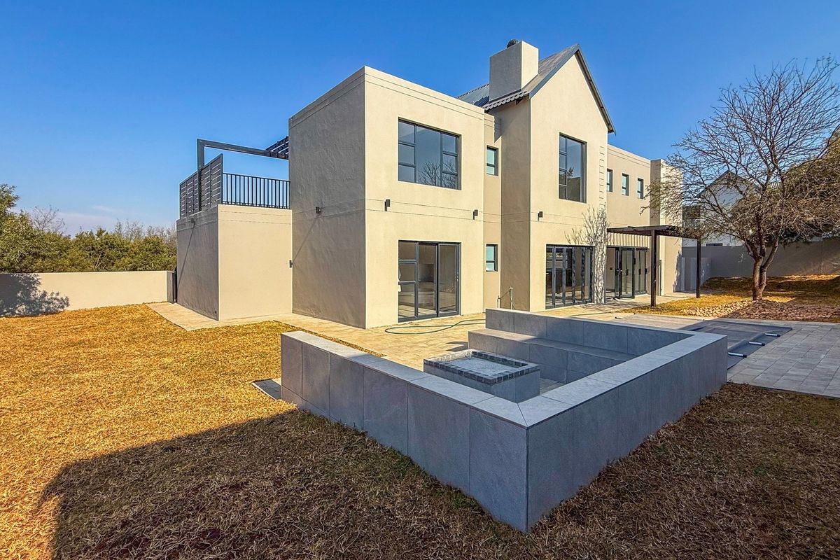 Rear view of a modern two-story house featuring a paved patio, built-in fire pit, and an upper-level balcony.