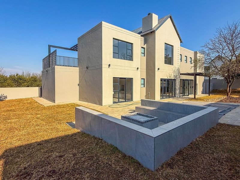 Rear view of a modern two-story house featuring a paved patio, built-in fire pit, and an upper-level balcony.