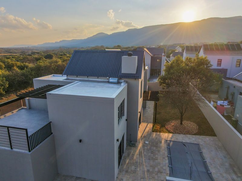 Aerial view of a modern residential property featuring a metal roof, swimming pool, paved patio area, and scenic mountain backdrop at sunset.