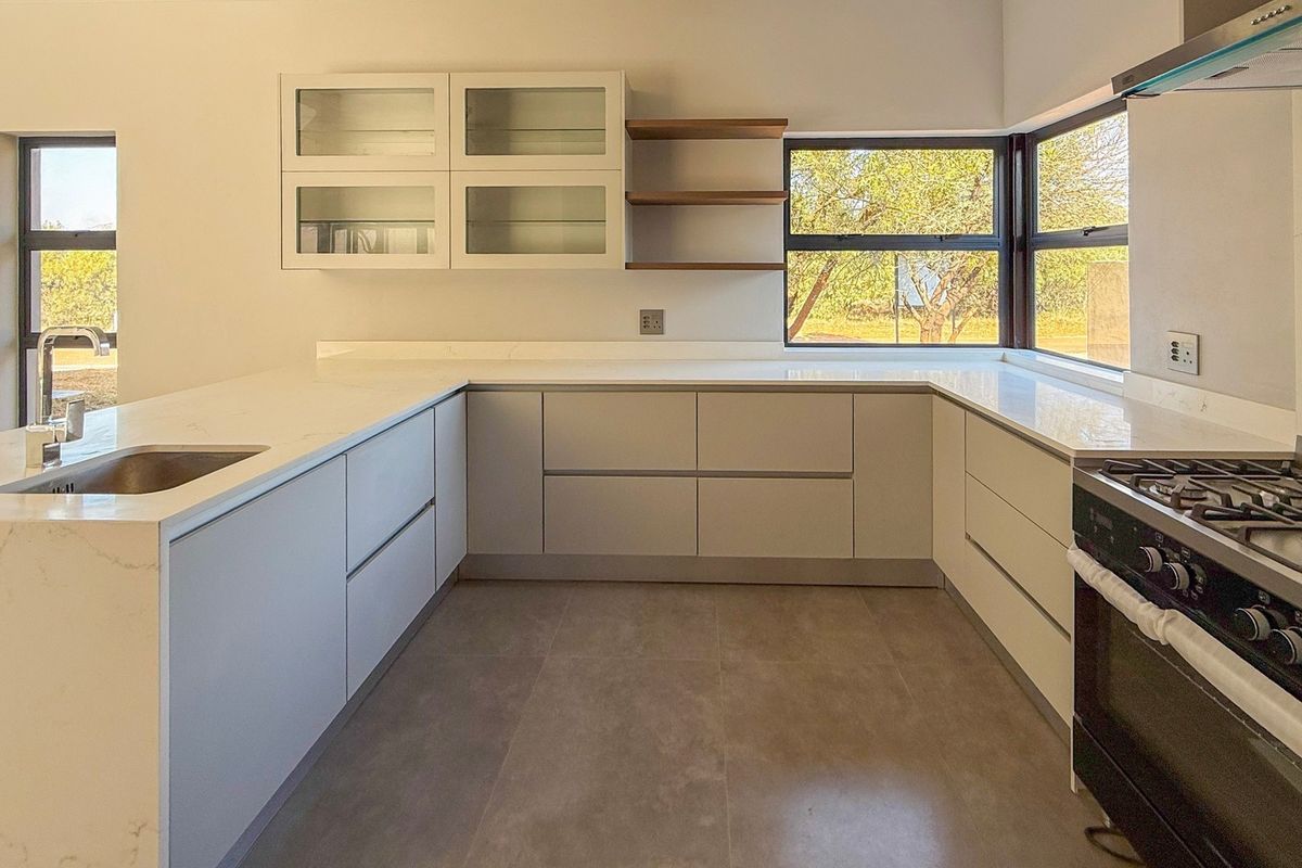 Modern kitchen featuring sleek handleless cabinetry, quartz countertops, integrated gas stove, extractor fan, and large windows providing ample natural light.