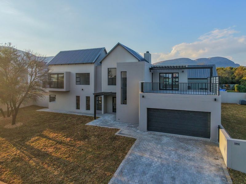 Modern double-story residence featuring a metal roof, integrated double garage, paved driveway, and an upper-level balcony with mountain views.