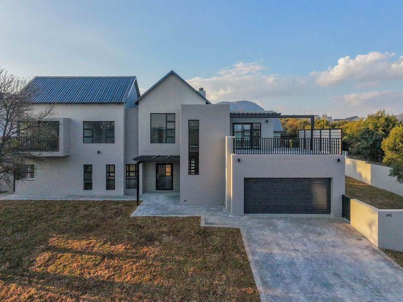 Modern two-story residential home featuring a metal roof, integrated double garage, paved driveway, and an upper-level balcony terrace.