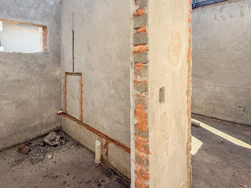 An unfinished utility space in shell condition, featuring exposed brickwork, plumbing rough-ins, and electrical conduits, ready for final interior finishes and fit-out.