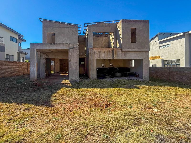 Rear view of a residential property currently under construction, featuring an unfinished concrete structure and surrounding brick boundary walls.