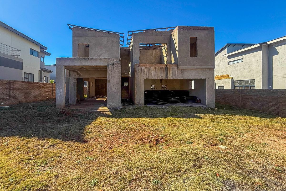 Rear view of a residential property currently under construction, featuring an unfinished concrete structure and surrounding brick boundary walls.