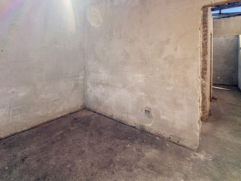 An unfinished interior space featuring exposed brickwork, plastered walls, and raw cement flooring, currently in a shell condition requiring full renovation.