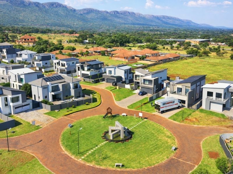 Aerial view of a modern residential estate featuring paved roads, a central landscaped roundabout, and contemporary homes with solar installations.