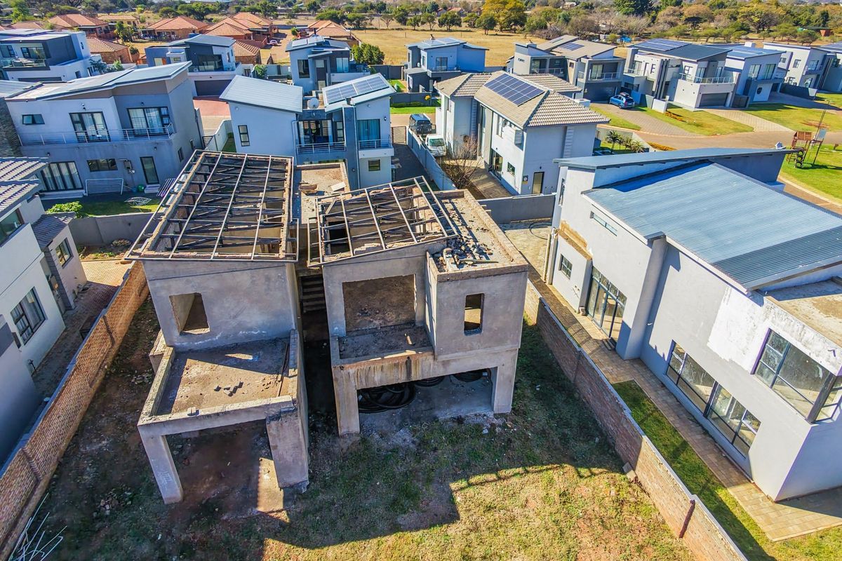 Aerial view of a residential property under construction, showing the concrete shell and exposed roof trusses within a developed estate.