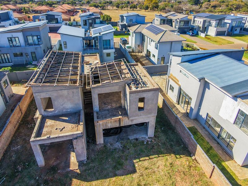 Aerial view of a residential property under construction, showing the concrete shell and exposed roof trusses within a developed estate.