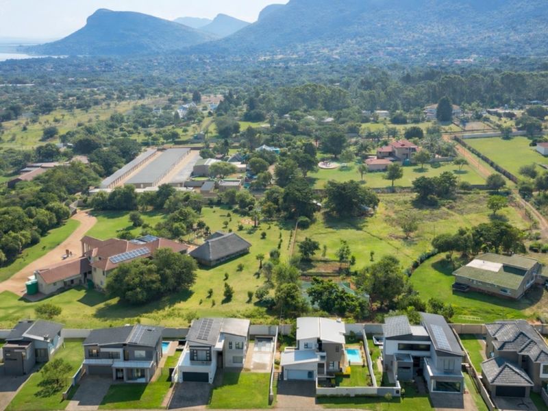 An aerial view of a modern residential estate featuring contemporary homes with solar panels, swimming pools, and landscaped gardens set against a scenic mountain backdrop.