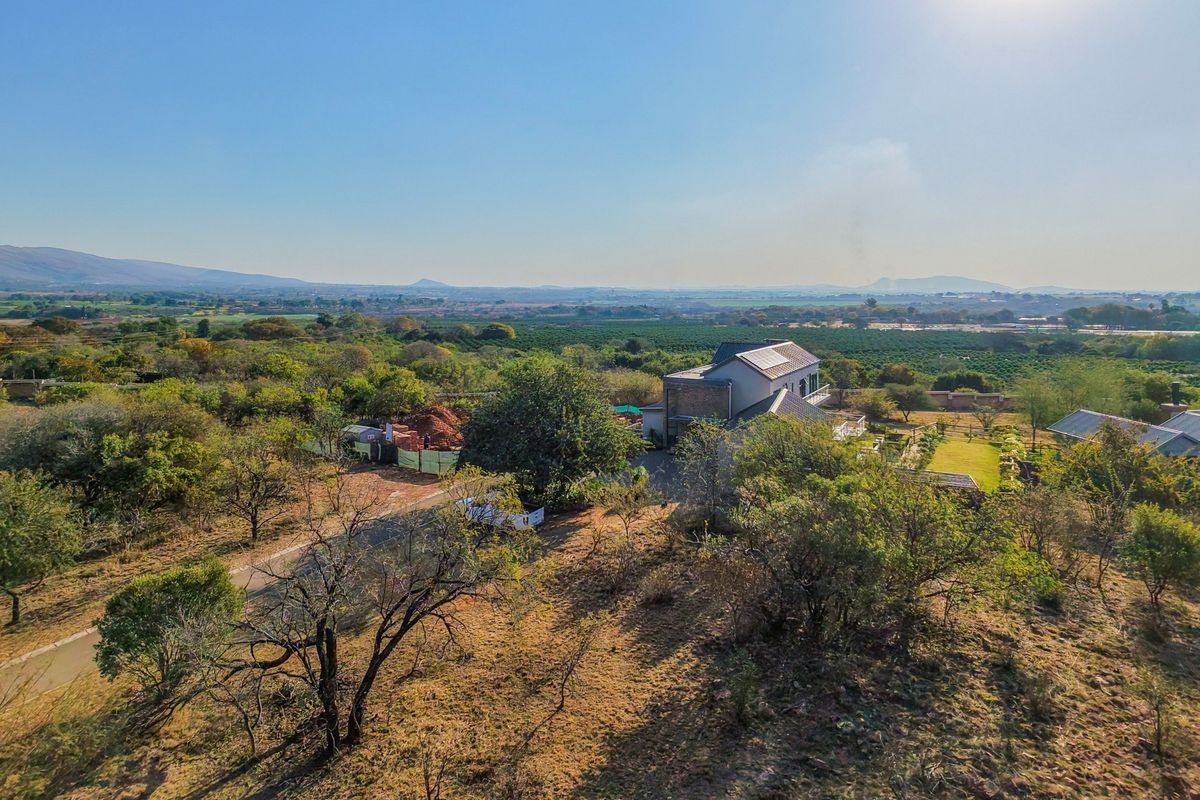 An aerial view of a residential property featuring a main dwelling with solar panels, surrounded by extensive landscaped grounds and natural vegetation.