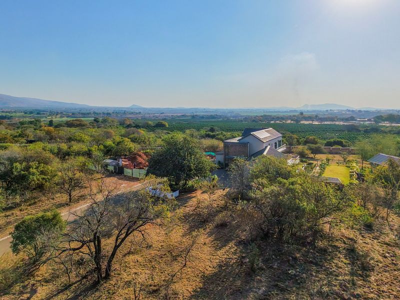 An aerial view of a residential property featuring a main dwelling with solar panels, surrounded by extensive landscaped grounds and natural vegetation.