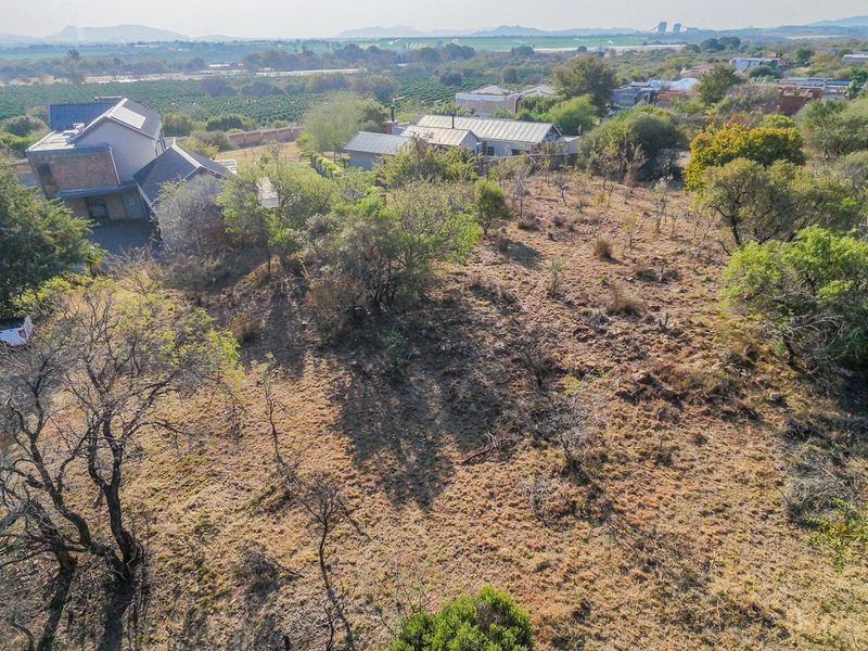 An aerial view of a vacant residential plot featuring natural vegetation, with established neighboring properties visible in the background.