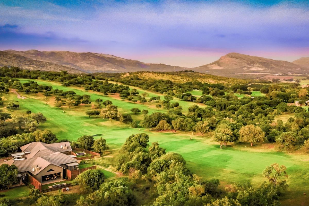 An elevated aerial view showcasing a residential property situated directly adjacent to a lush, expansive golf course with scenic mountain vistas in the background.