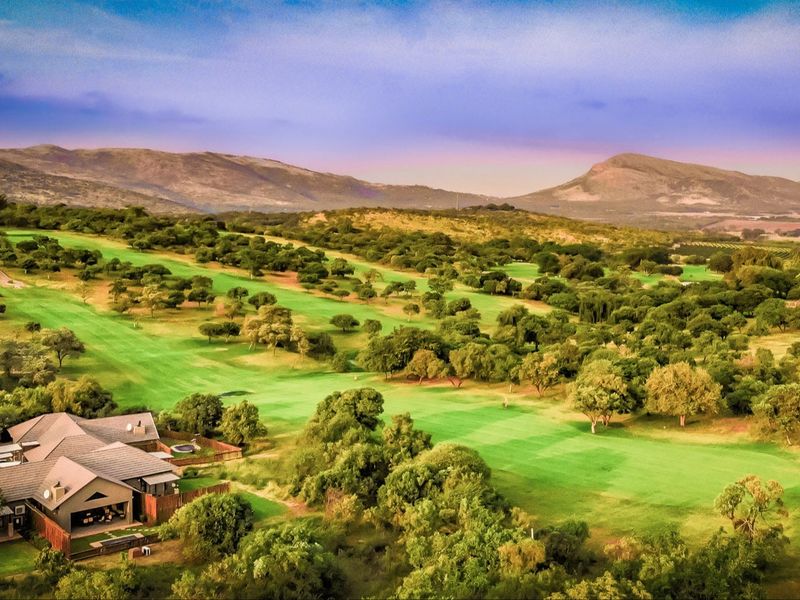 An elevated aerial view showcasing a residential property situated directly adjacent to a lush, expansive golf course with scenic mountain vistas in the background.