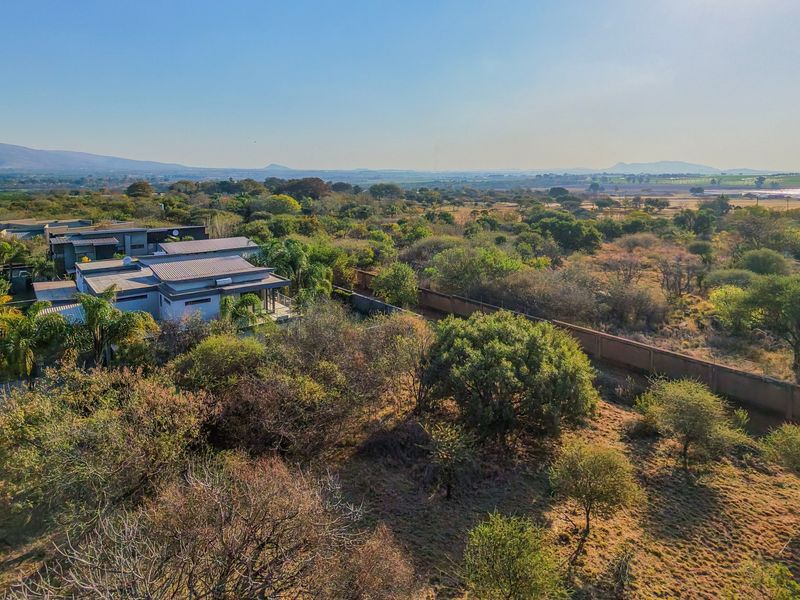 Aerial view of a residential plot featuring native vegetation, a perimeter wall, and proximity to established housing and local road infrastructure.
