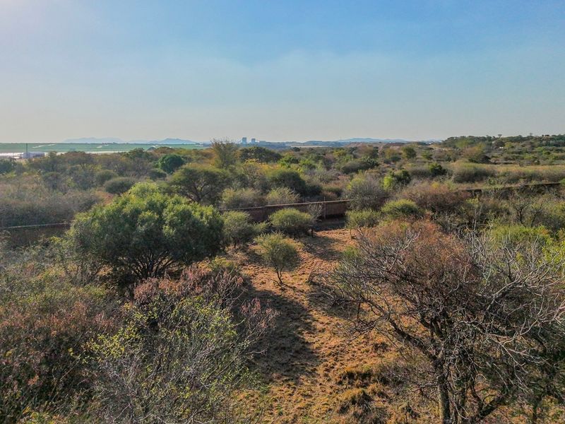 An aerial view of a vacant residential plot featuring natural vegetation and perimeter fencing, offering a clear perspective of the land's landscape.