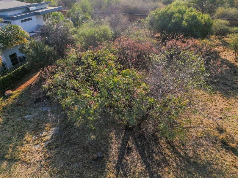 An aerial view of a residential vacant land plot featuring established trees and natural vegetation, adjacent to an existing residential property.