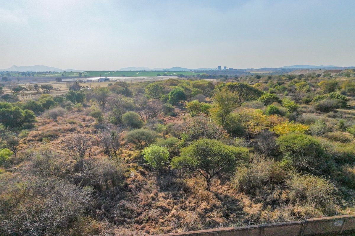 An aerial view of a vacant residential plot featuring natural vegetation and perimeter fencing, offering expansive views of the surrounding landscape.