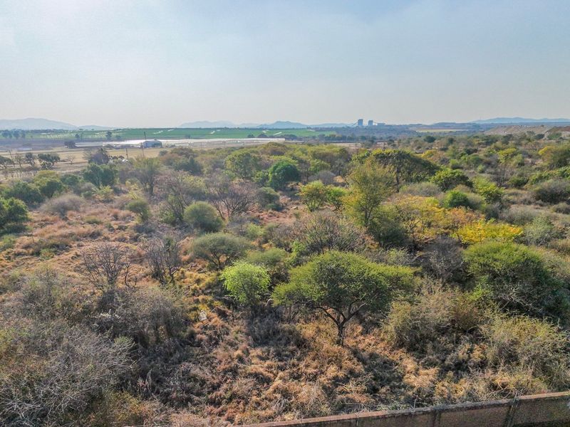 An aerial view of a vacant residential plot featuring natural vegetation and perimeter fencing, offering expansive views of the surrounding landscape.