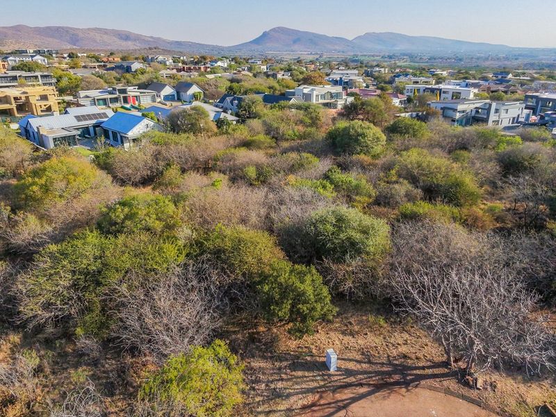 Aerial view of a vacant residential plot featuring natural vegetation and surrounding established estate housing with mountain views.