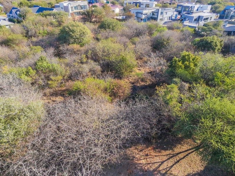 An aerial view of a vacant residential plot featuring natural indigenous vegetation and surrounding established residential properties.