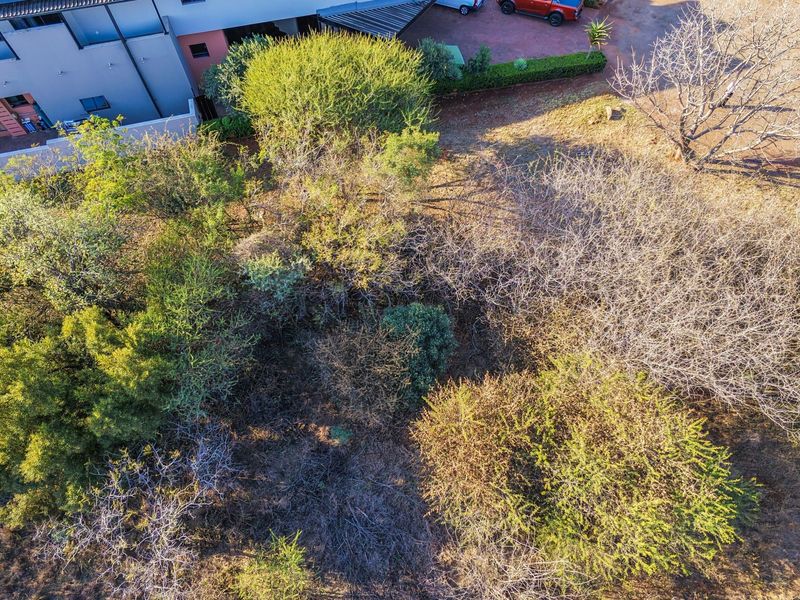 An aerial view of a vacant residential plot featuring established native trees and natural vegetation, adjacent to existing residential development.
