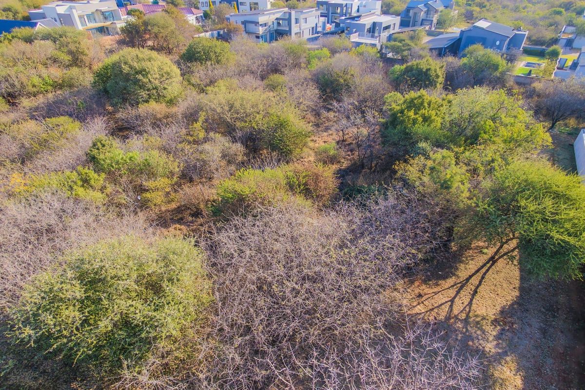 An aerial view of a vacant residential plot featuring dense native vegetation and mature trees, situated within an established residential estate.