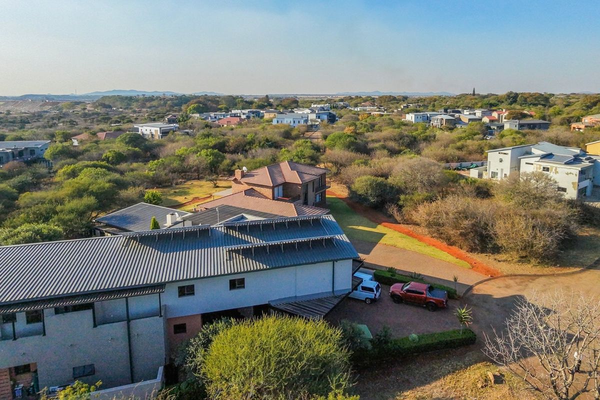 Aerial view of a residential property within a landscaped estate, featuring a metal roof structure and paved driveway access.