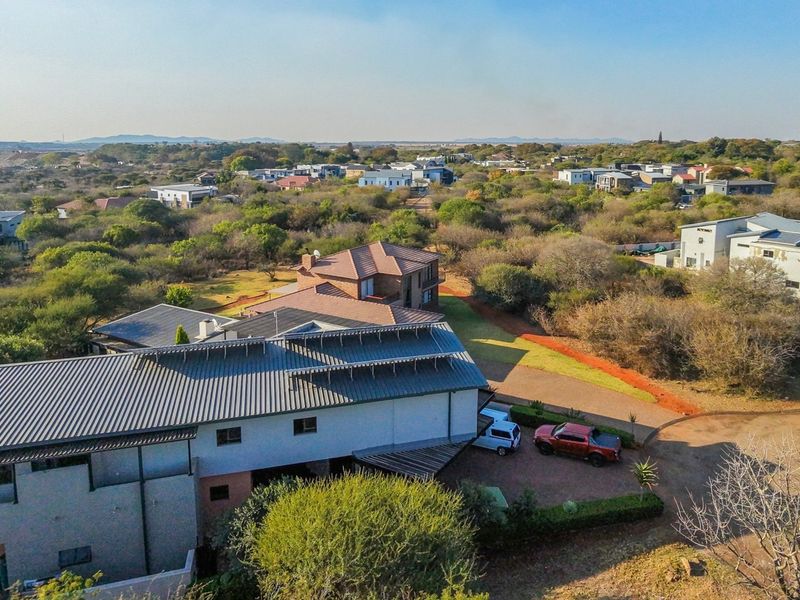 Aerial view of a residential property within a landscaped estate, featuring a metal roof structure and paved driveway access.