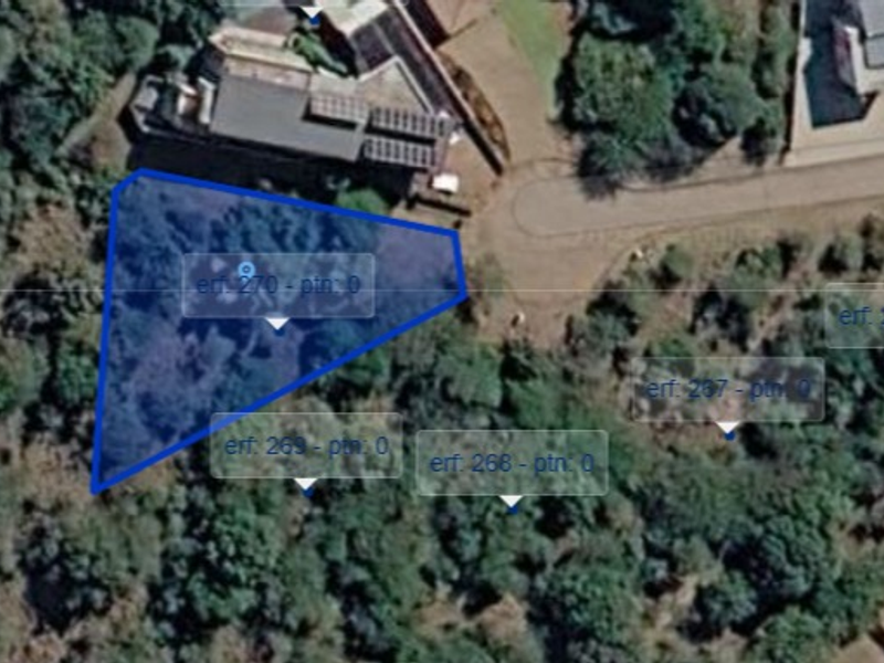 An aerial view of a vacant residential plot of land, highlighted in blue, surrounded by established trees and nearby residential properties.
