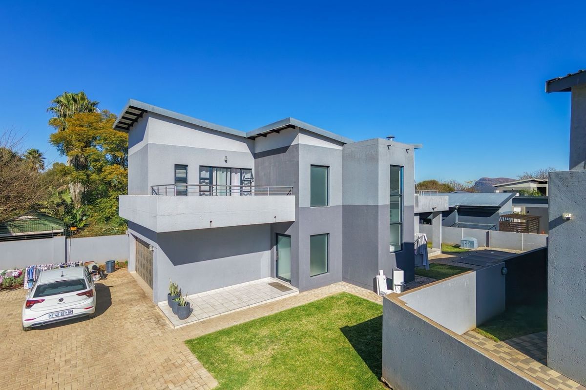 Aerial view of the rear elevation featuring a modern two-story house with a paved driveway, balcony, and private garden area.