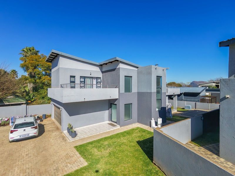 Aerial view of the rear elevation featuring a modern two-story house with a paved driveway, balcony, and private garden area.