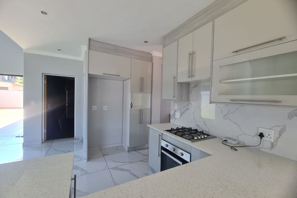Modern kitchen featuring sleek built-in cabinetry, stone countertops, a gas hob, and a built-in oven with elegant marble-look splashback tiling.