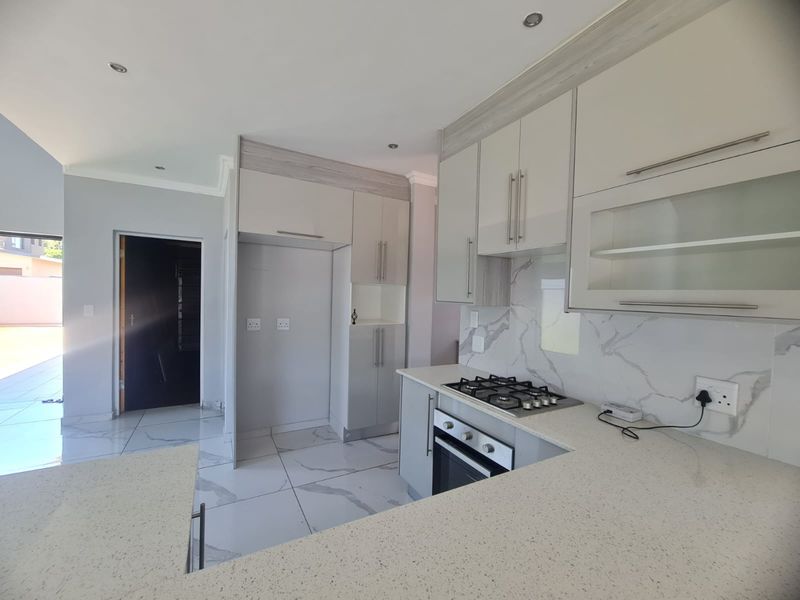 Modern kitchen featuring sleek built-in cabinetry, stone countertops, a gas hob, and a built-in oven with elegant marble-look splashback tiling.