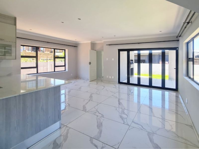 Spacious open-plan living area featuring modern marble-look floor tiles, recessed lighting, and large aluminium stacker doors leading to the outdoor patio.