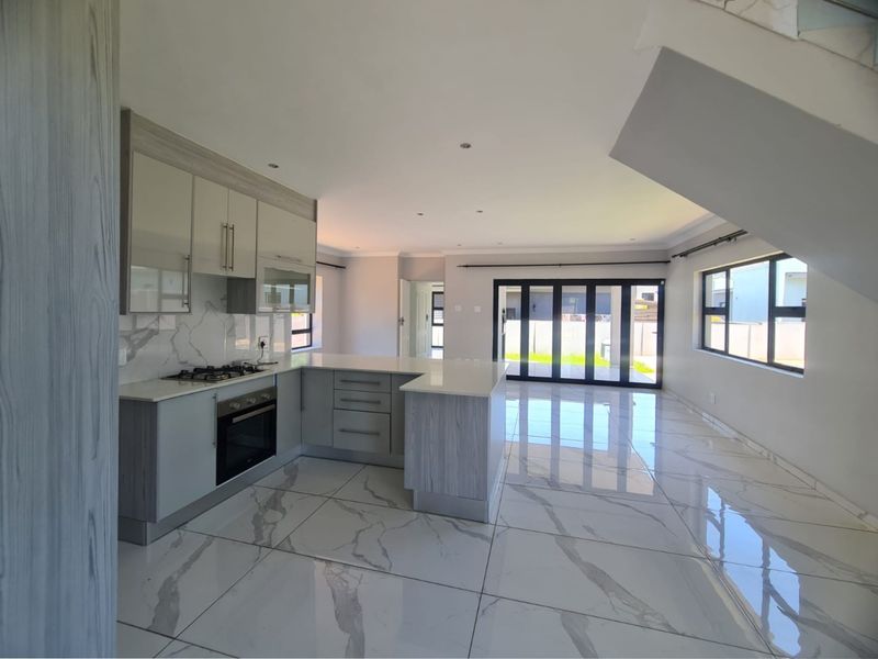 Modern open-plan kitchen and living area featuring marble-look floor tiles, sleek cabinetry, built-in appliances, and large stacker doors leading to the garden.