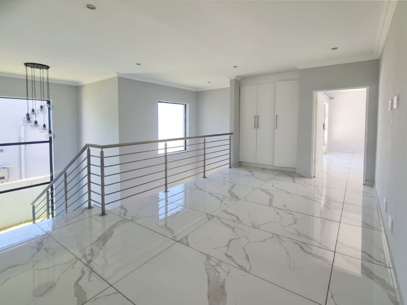 A bright, modern landing area featuring polished marble-look floor tiles, a sleek stainless steel balustrade, and ample built-in storage cabinetry.