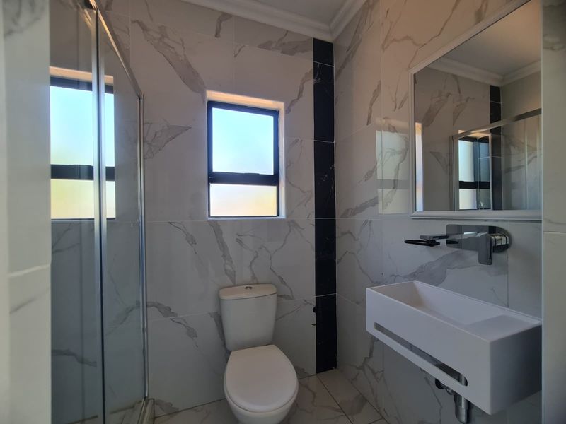 Modern bathroom featuring marble-look wall tiles, a glass shower enclosure, a wall-mounted basin, and a toilet.